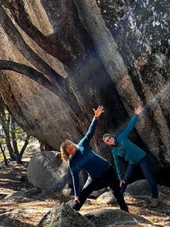 Two women are doing yoga in front of a large tree.