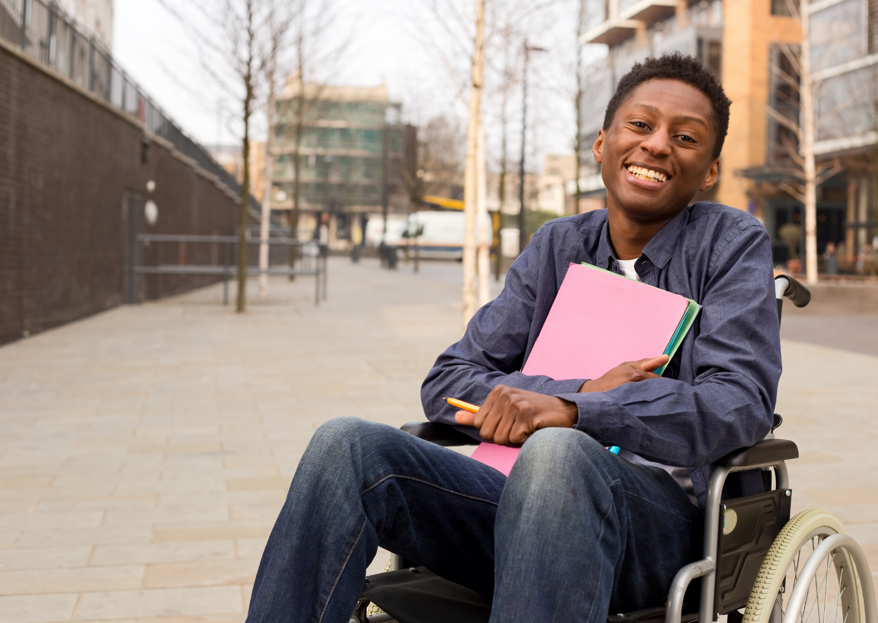 a man in a wheelchair is smiling and holding a pink folder .