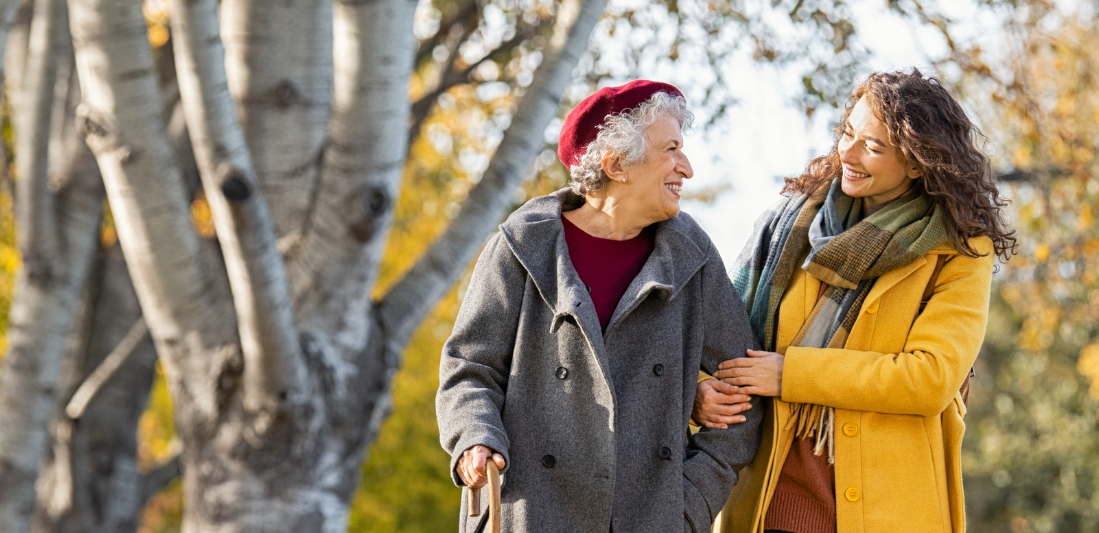 A young woman is helping an older woman walk in a park.