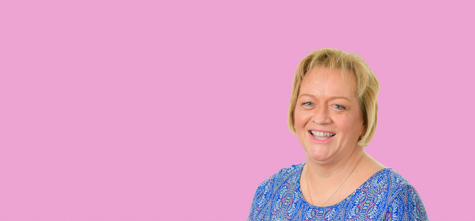 a woman in a blue shirt is smiling on a pink background .