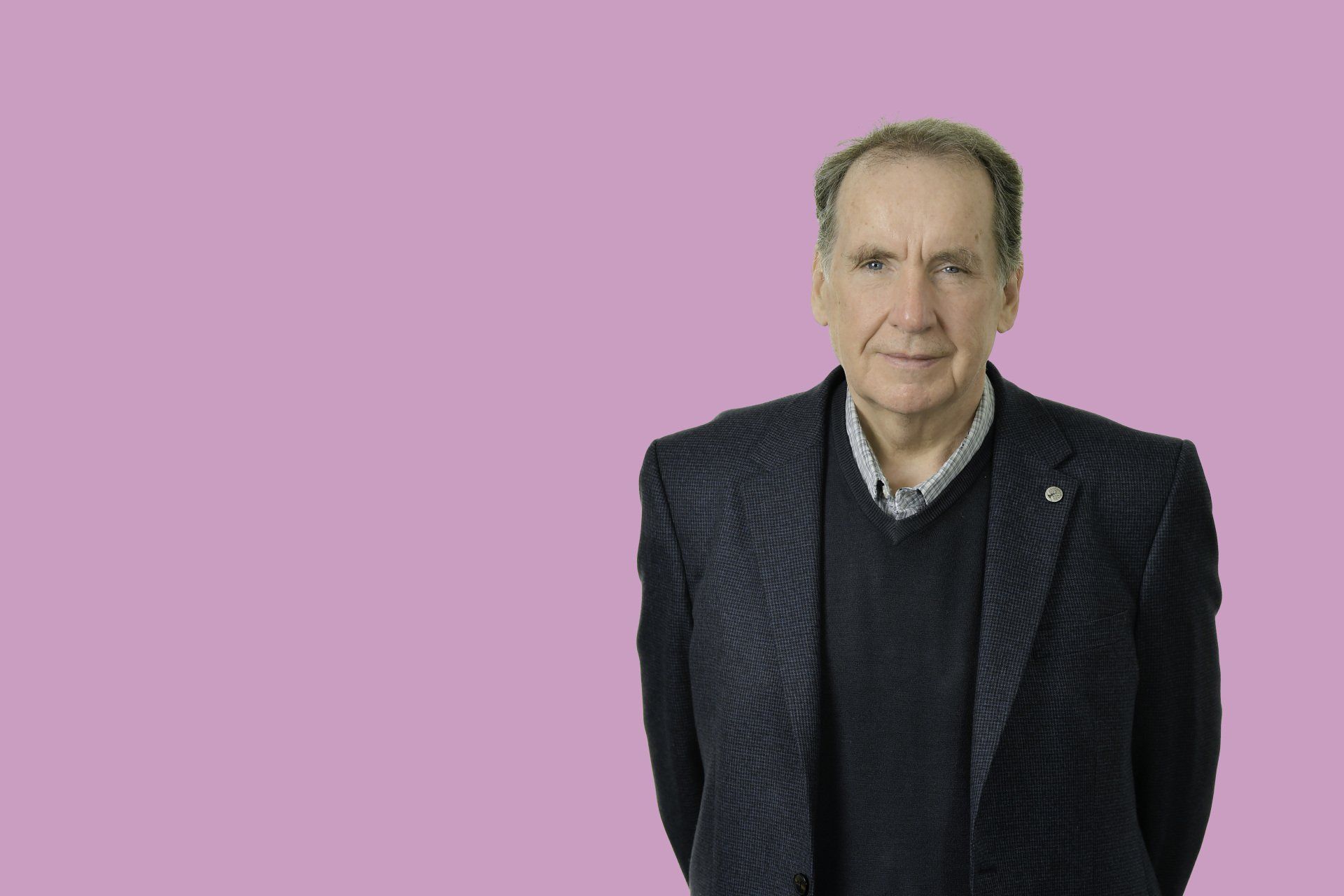 a man in a suit and sweater is standing in front of a pink background .