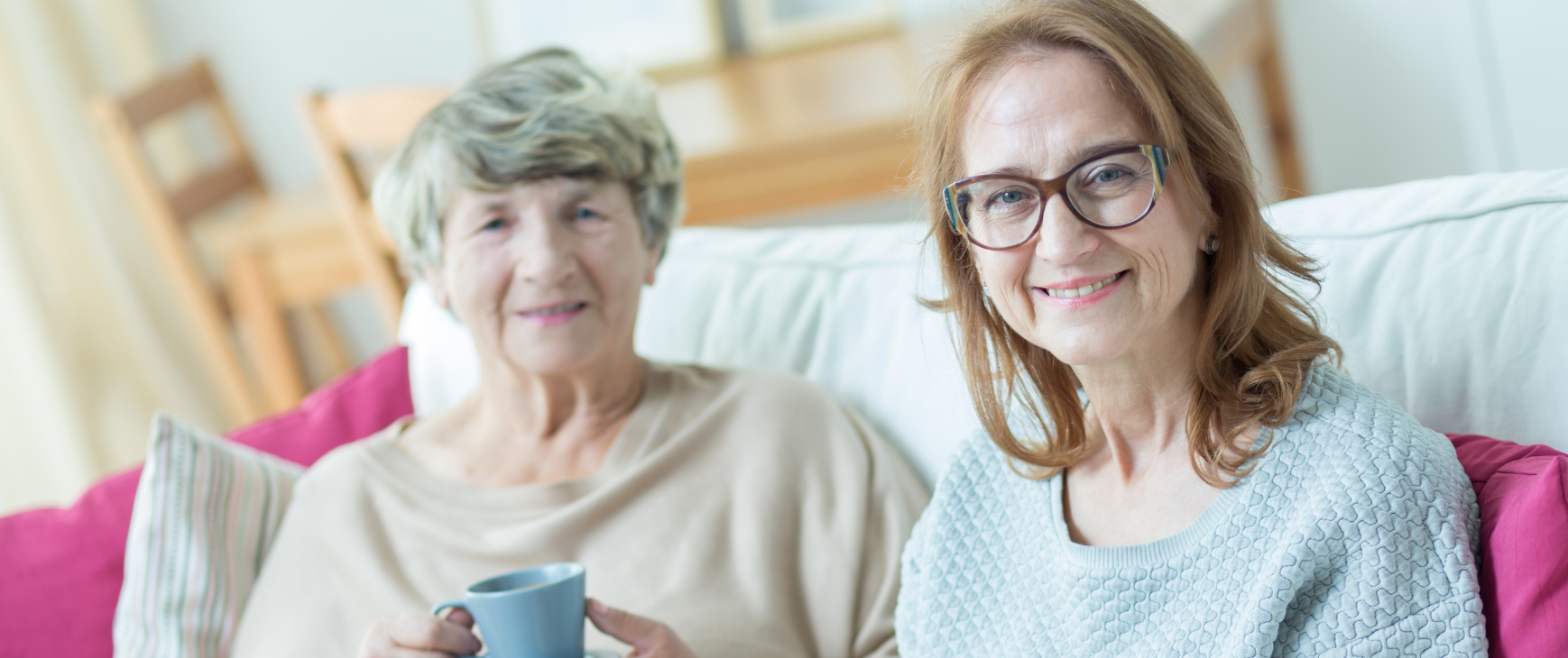 two women are sitting on a couch holding cups of coffee .