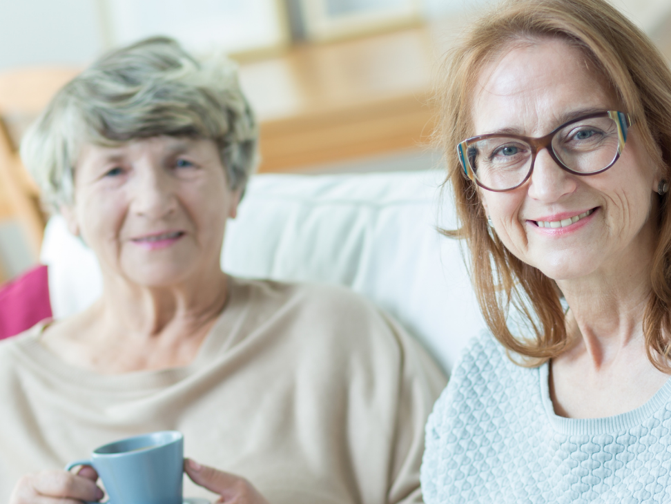 two women are sitting on a couch holding cups of coffee .