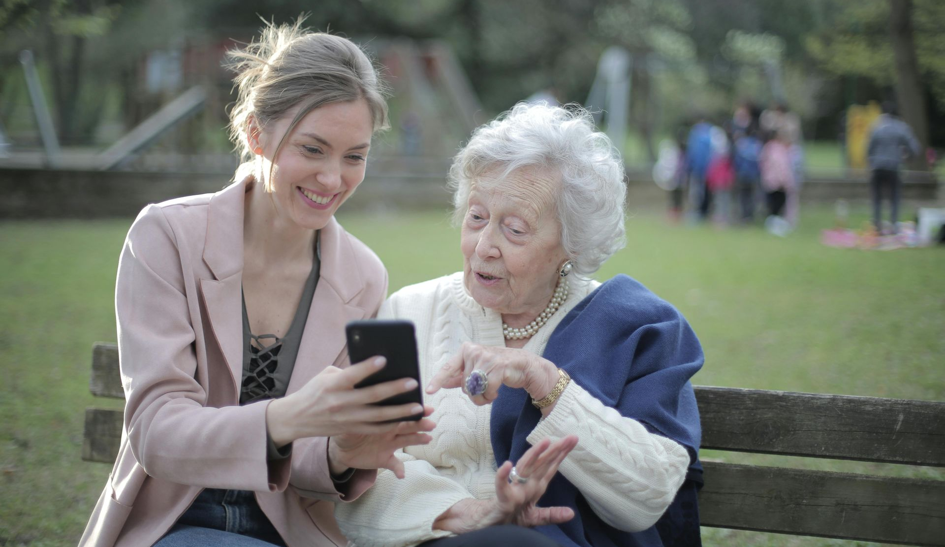 two women on a bench in the park, looking at a mobile phone