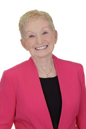 A woman in a pink jacket and black shirt is smiling.