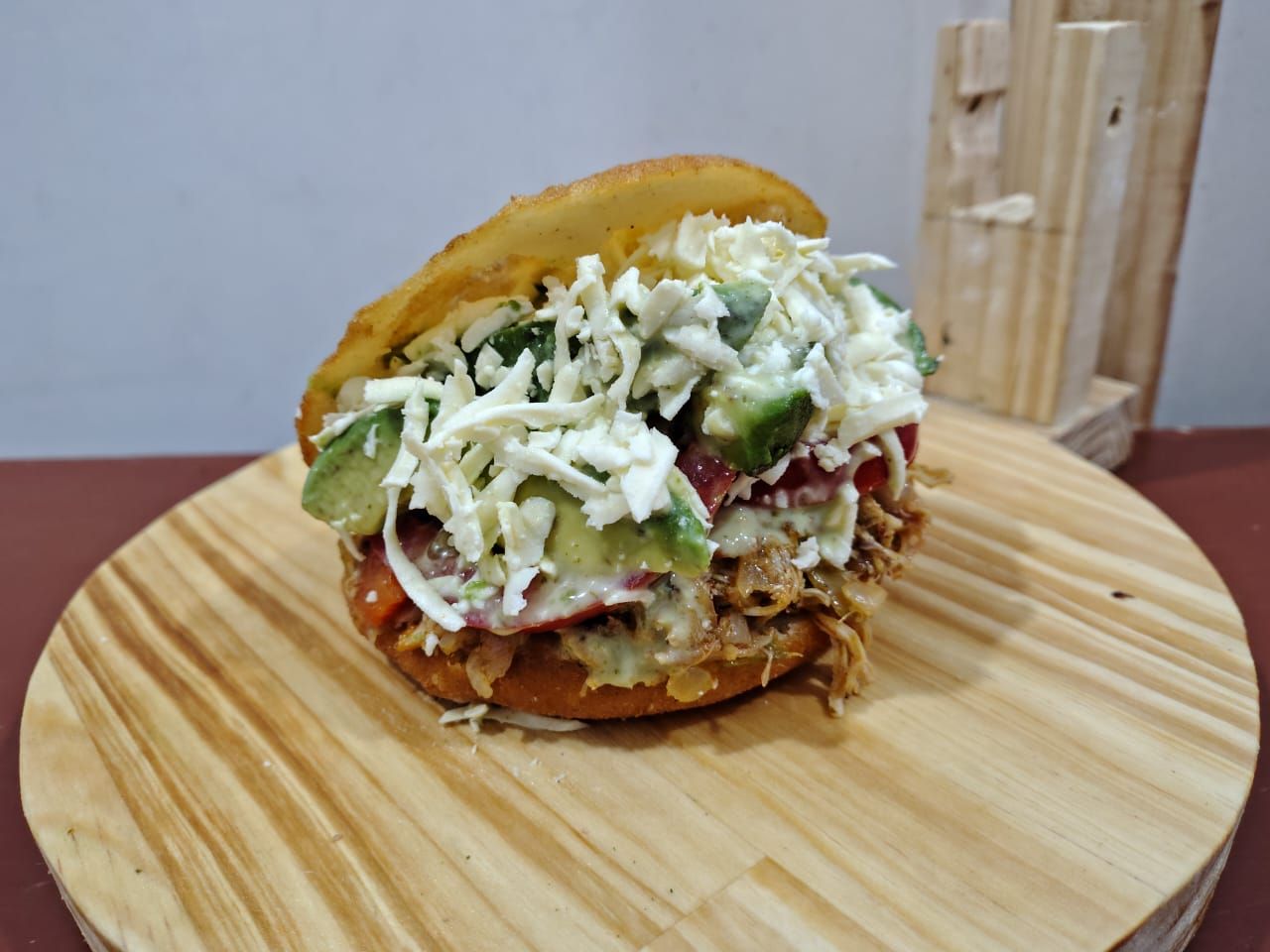 Arepa rellena de carne desmenuzada, aguacate, queso rallado y ensalada de col, sobre una tabla de madera.
