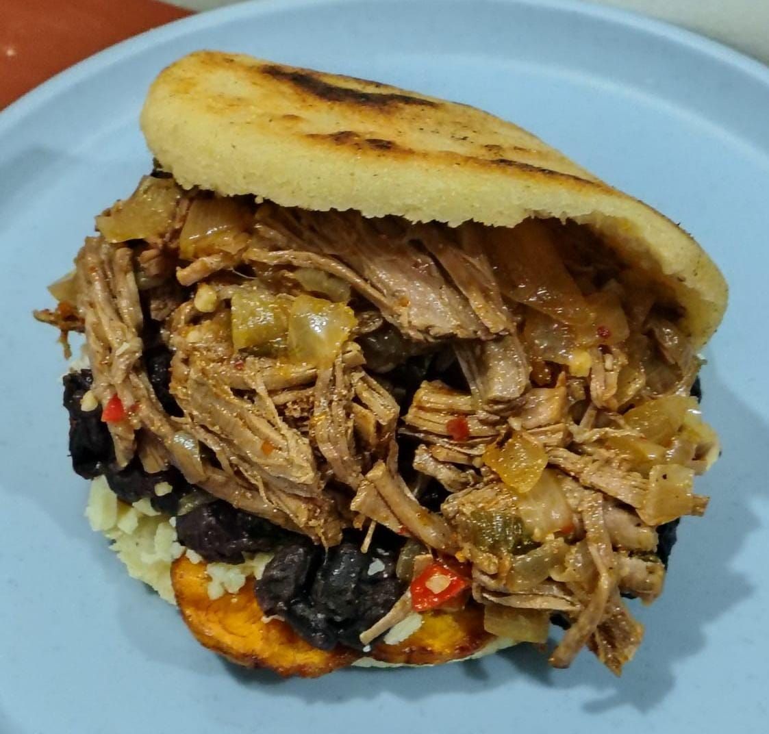 Arepa rellena de carne deshebrada, frijoles negros y plátanos, en un plato azul.