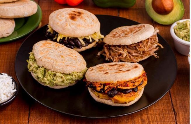 Arepas con diversos rellenos en plato negro: frijoles negros, carne deshebrada, aguacate y plátanos.