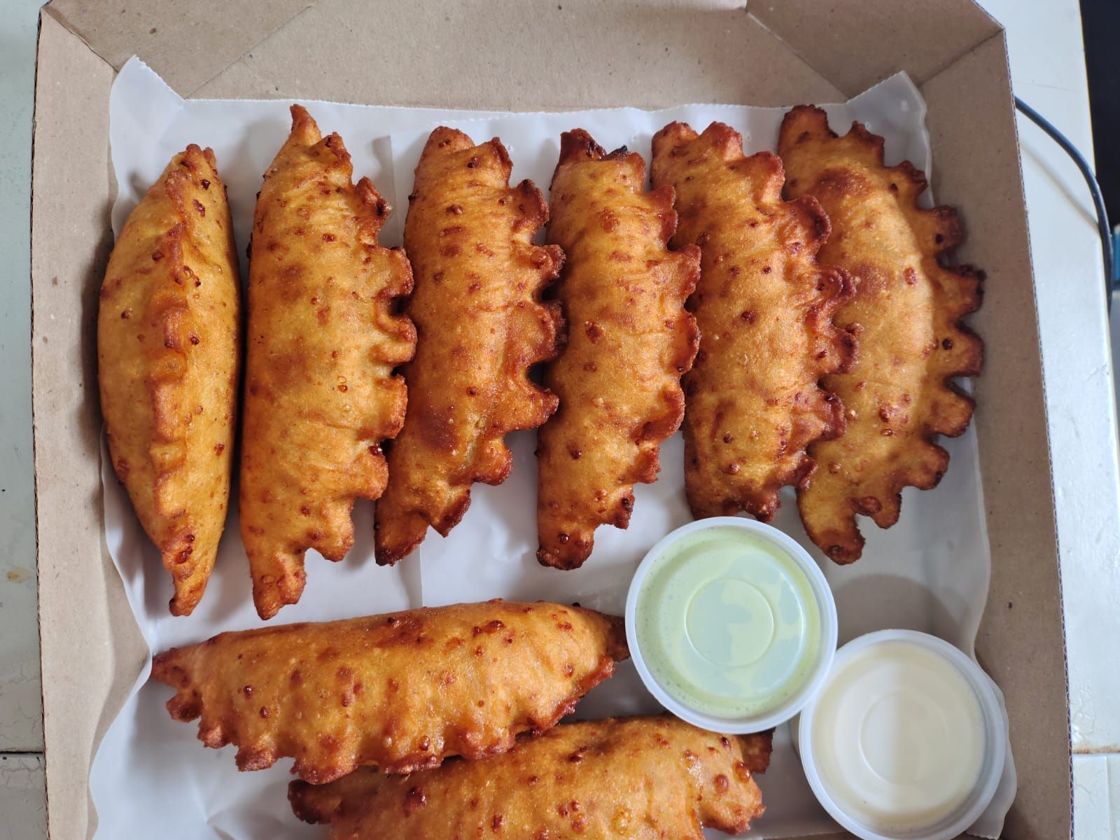 Caja de empanadas fritas con dos salsas para mojar.