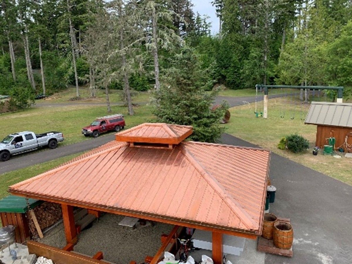 Wooden pavilion with metal roof in a yard, trucks and trees in the background. Wooden pavilion with metal roof in a yard, trucks and trees in the background.