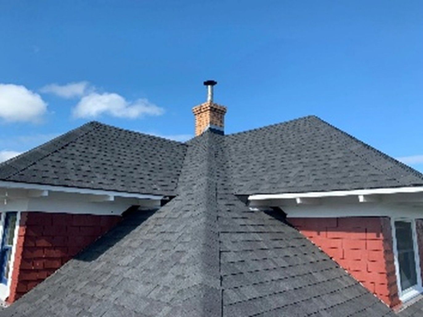 Gray shingle roof with a brick chimney against a clear blue sky. Gray shingle roof with a brick chimney against a clear blue sky.