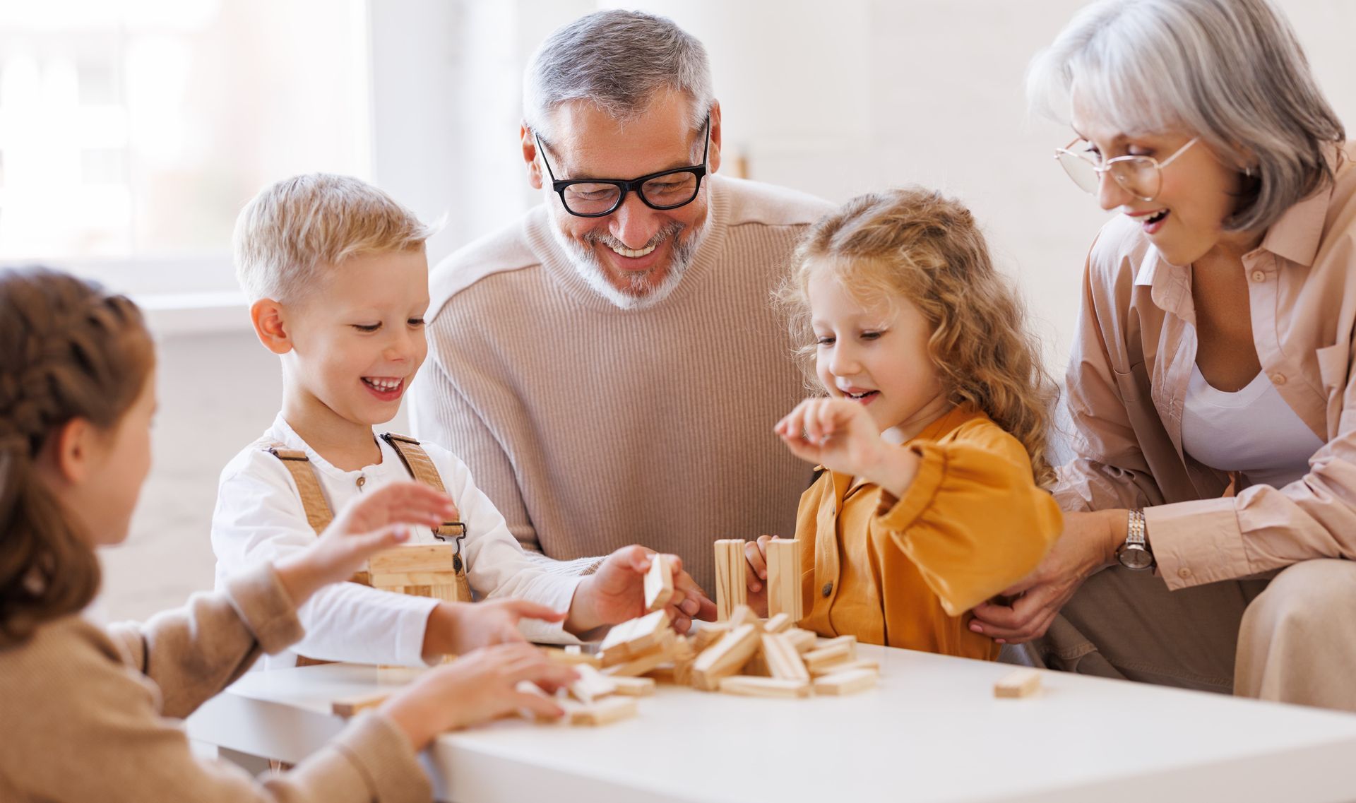 Grandparents and grandchildren playing a tower game together at a table. They are smiling.