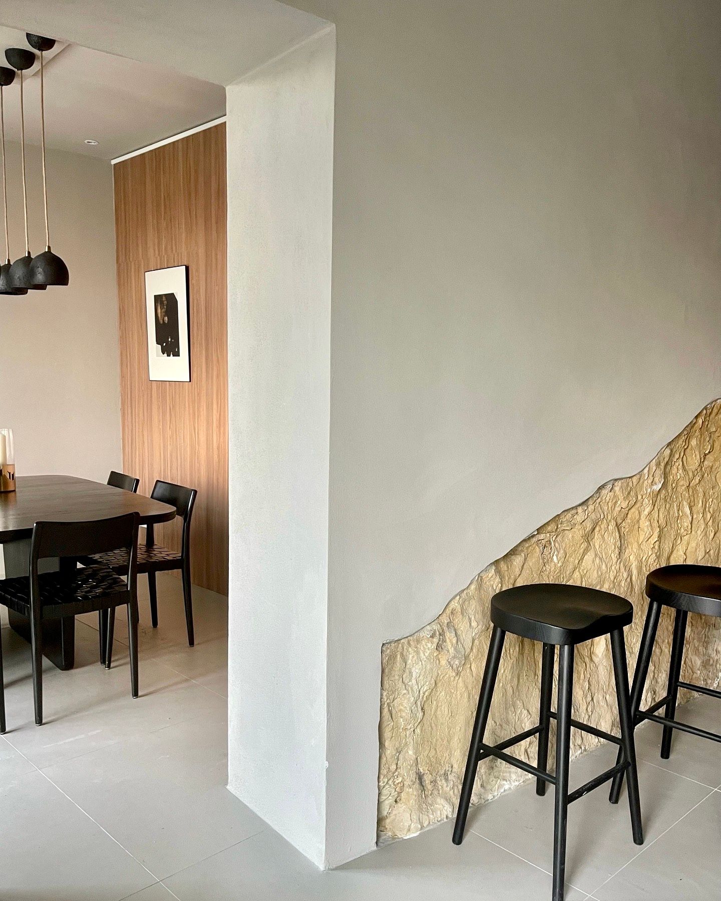 Modern dining room with dark table and chairs; a partially textured wall with stools.