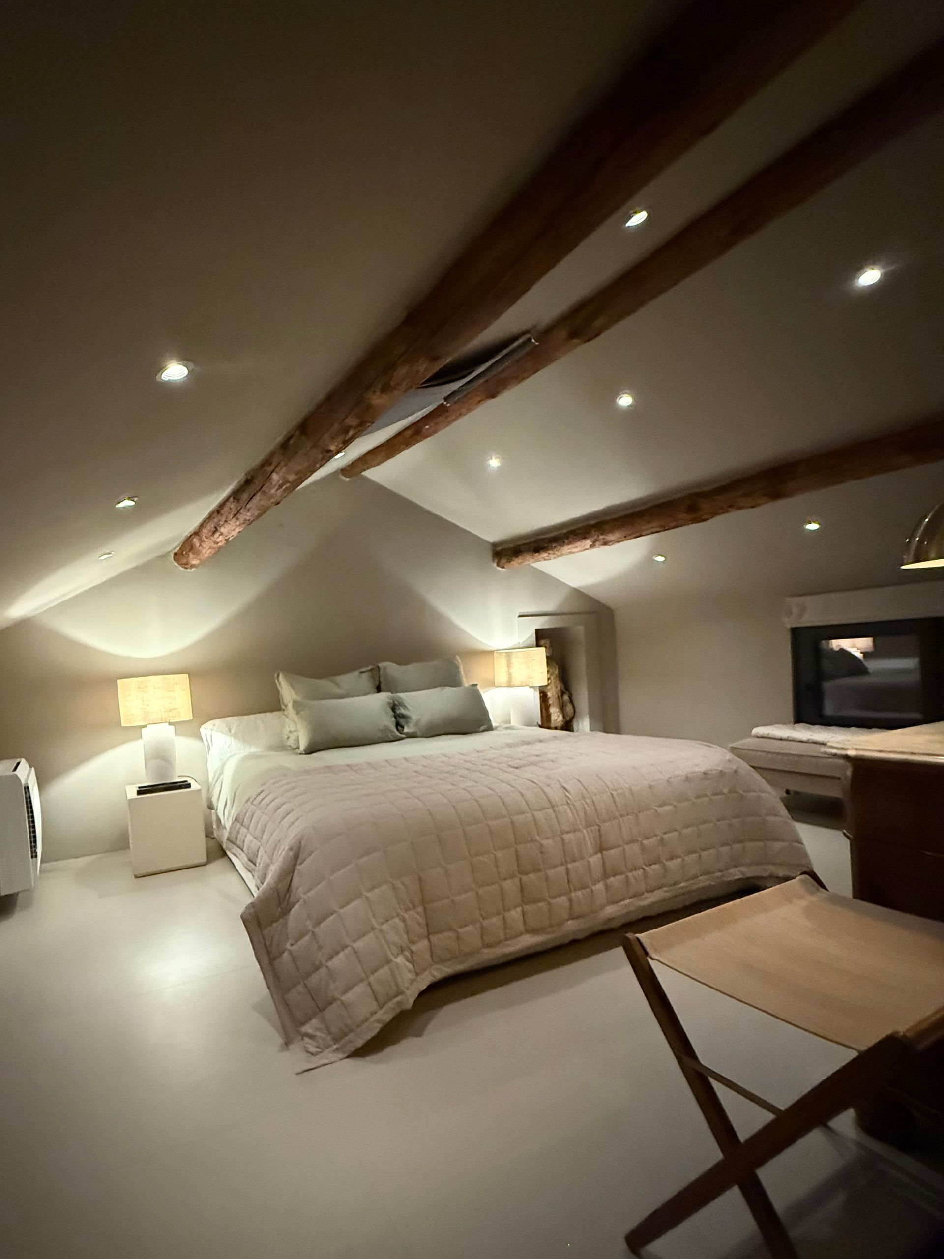 Bedroom with angled ceiling, bed, wooden beams, bedside tables, and a small desk.