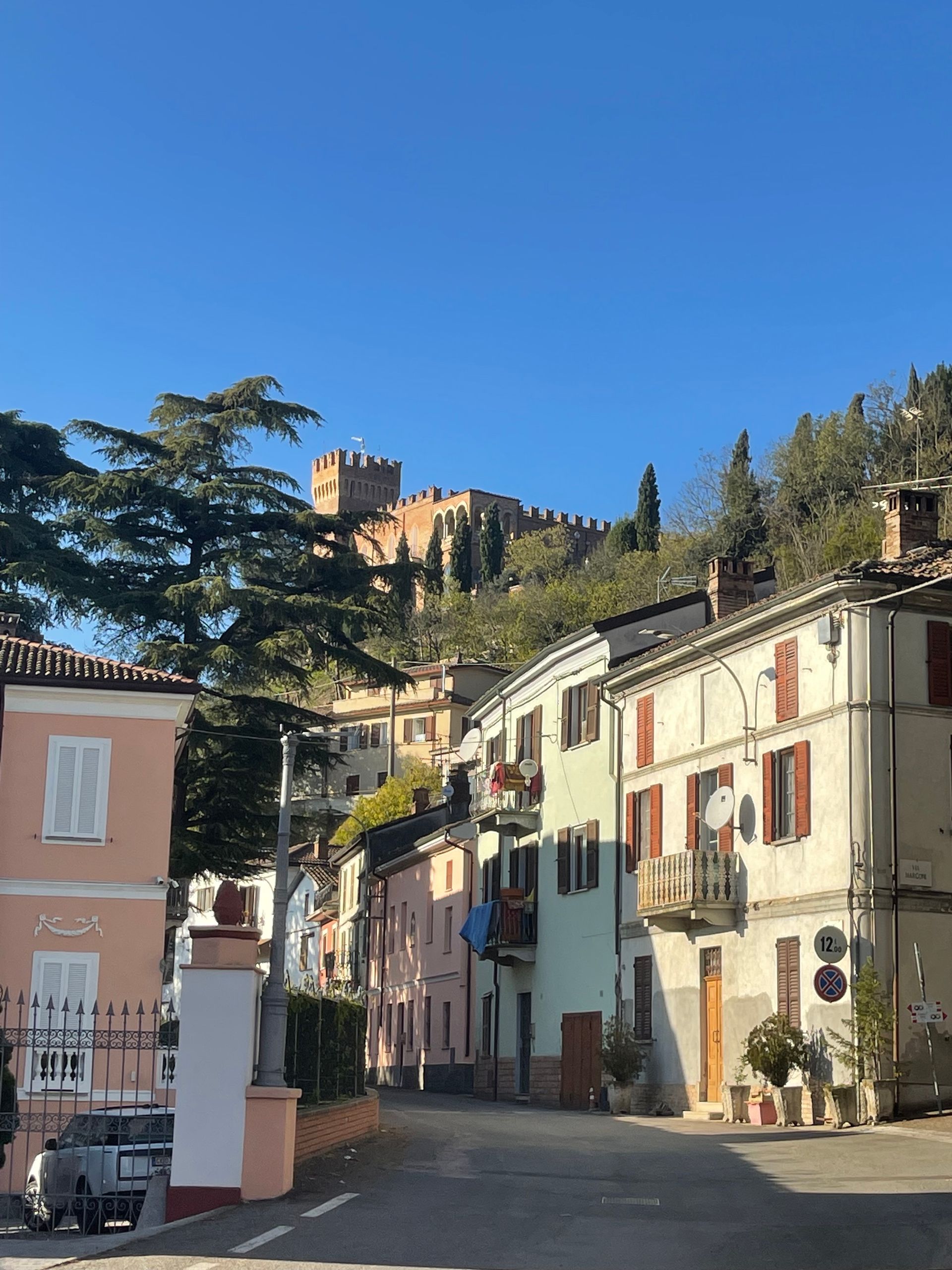Street view of Italian town with colorful buildings and a hilltop castle.