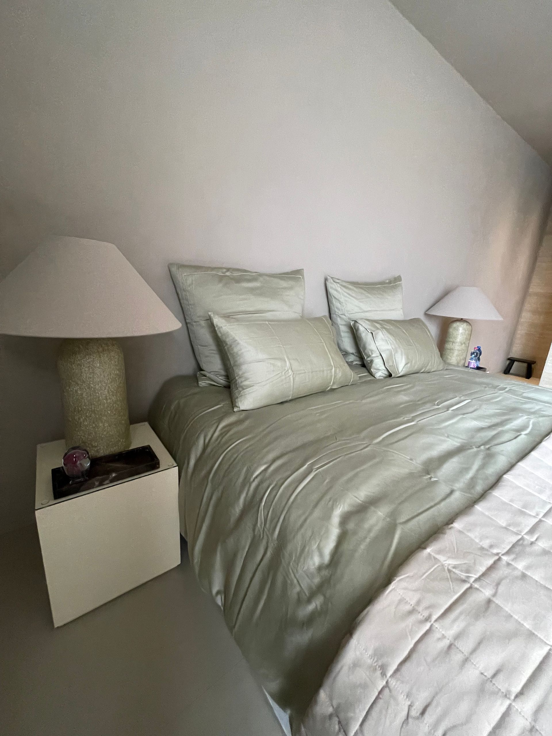 Bedroom with pale green bedding and pillows, bedside lamps on white nightstands.