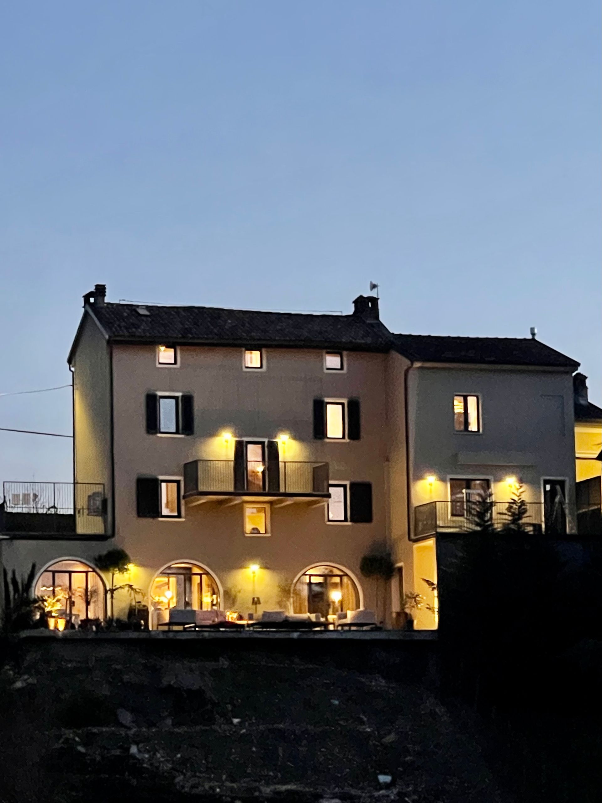 Beige building with arched windows lit up at dusk, set on a hillside.