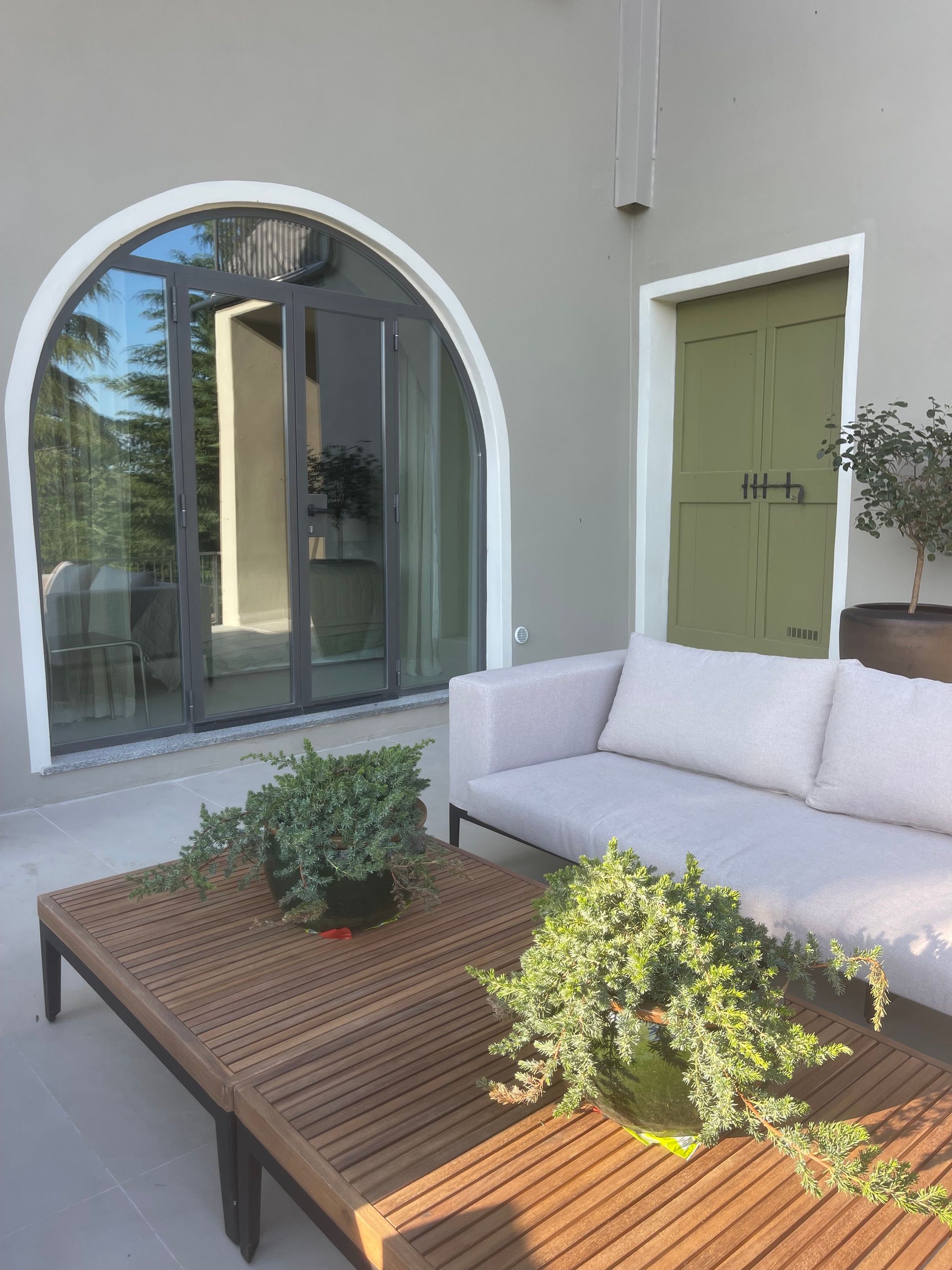 Outdoor patio with a white sofa, wooden table, and arched glass doors, light green door.