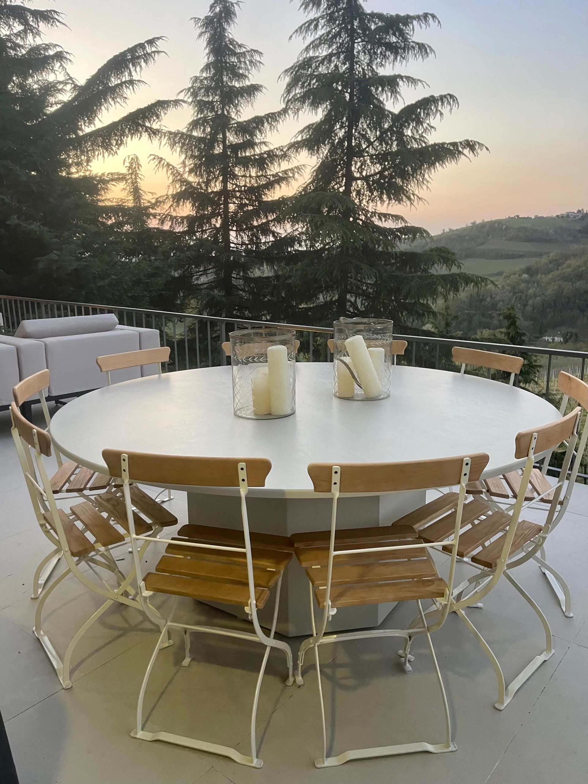 Round outdoor table with wooden chairs, set against a scenic landscape at sunset.