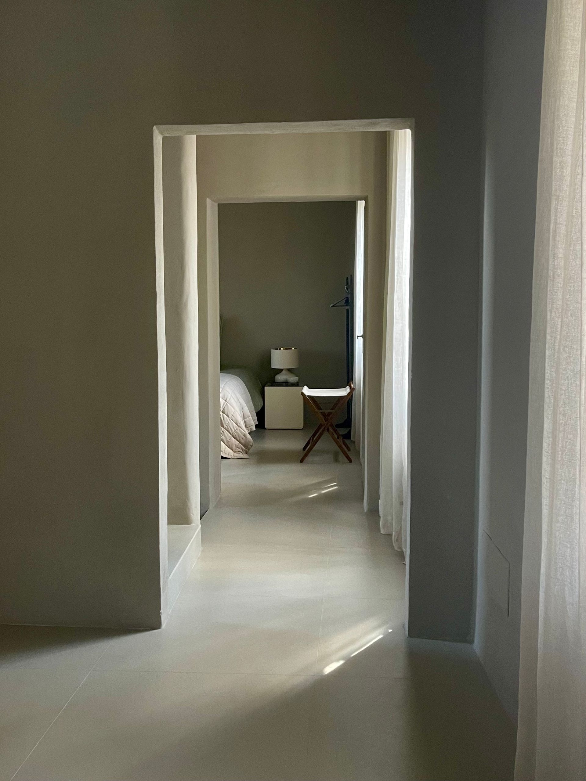 Hallway view into a bedroom. Light streams in through sheer curtains. Neutral color palette.