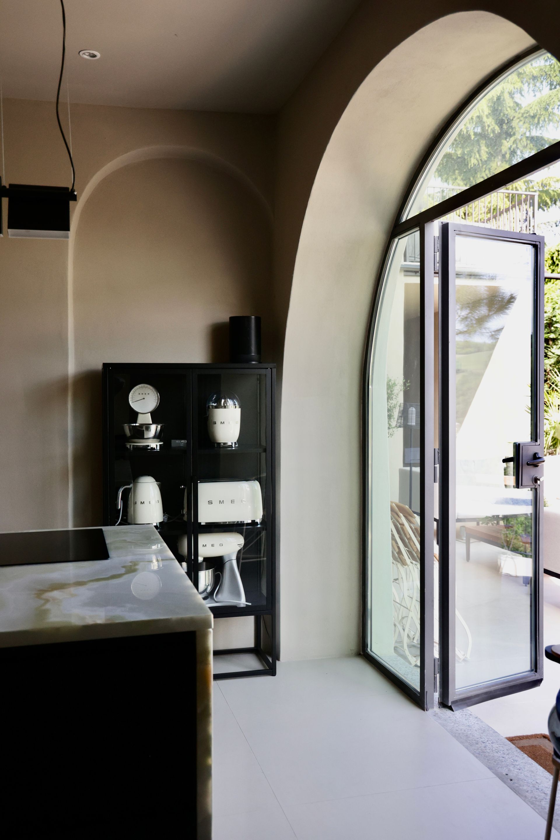 Dining room with marble table, black pendant lights, vase with white flowers, and a dark cabinet.