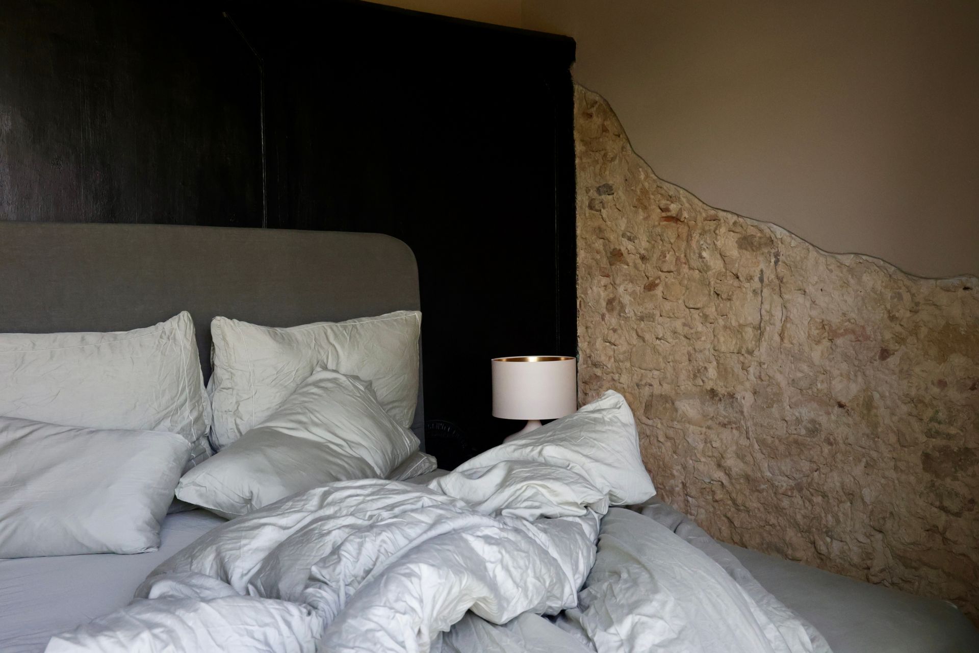 Bed with rumpled white comforter, pillows, and gray headboard against a dark closet and textured wall.