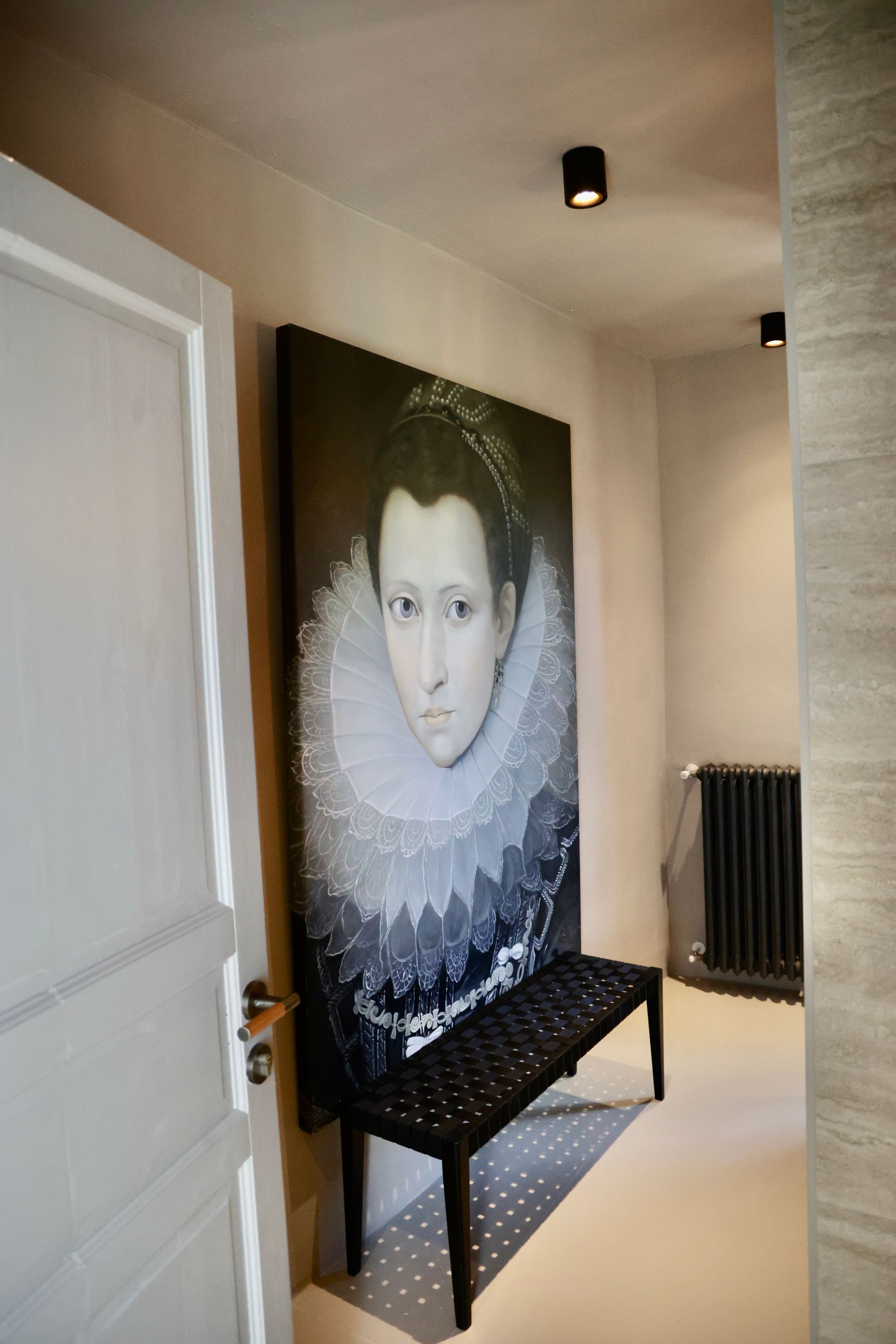 A large portrait of a Eleonora Gonzaga in a frilly collar hangs above a black bench in a hallway.