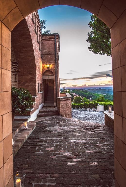 Brick castle courtyard framed by an arch, overlooking a sunset view.
