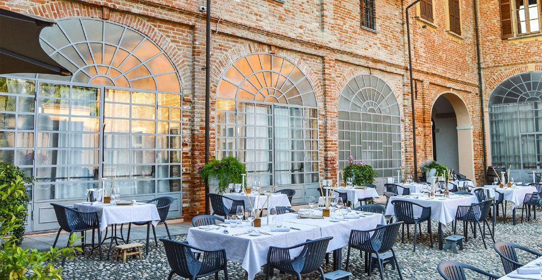 Outdoor dining area with tables set for a meal, brick walls, and large arched windows.