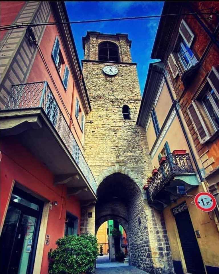 Clock tower archway between colorful buildings; sunny sky.