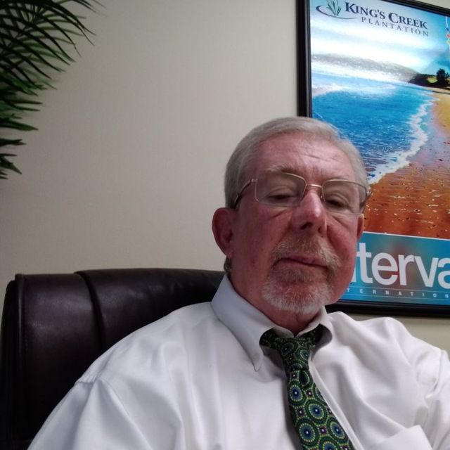A man in a suit and white shirt is leaning against a wall.