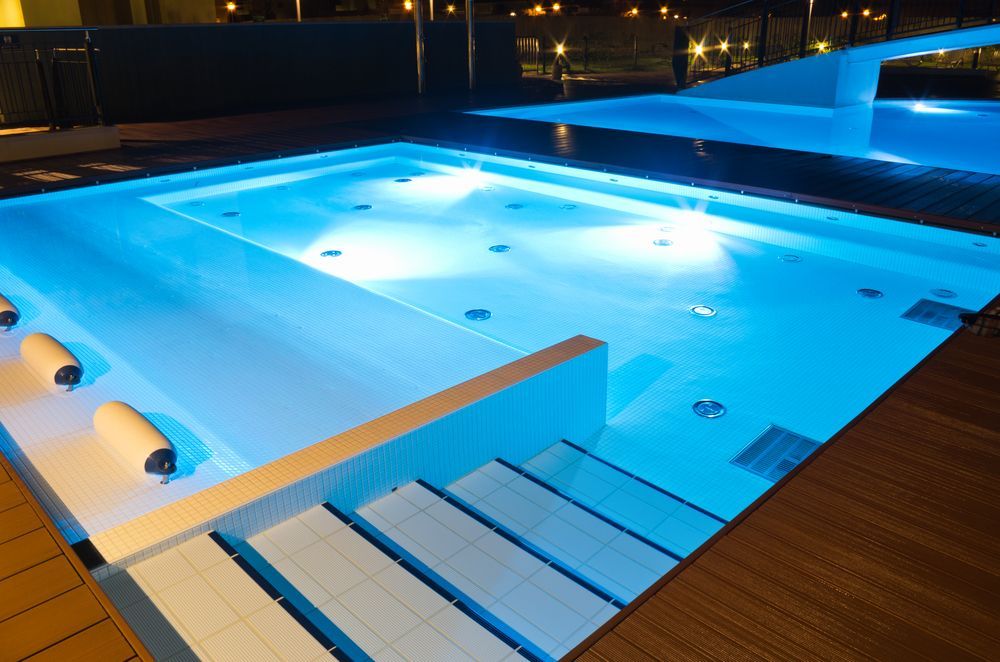 A Large Swimming Pool Is Lit up At Night — Sun Cool Pools & Spas in Maryborough, QLD