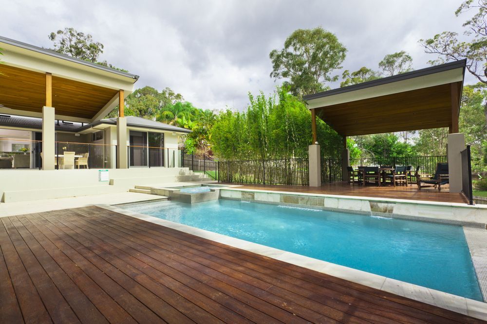 A Large Swimming Pool with A Wooden Deck in Front of A House — Sun Cool Pools & Spas in Gympie, QLD