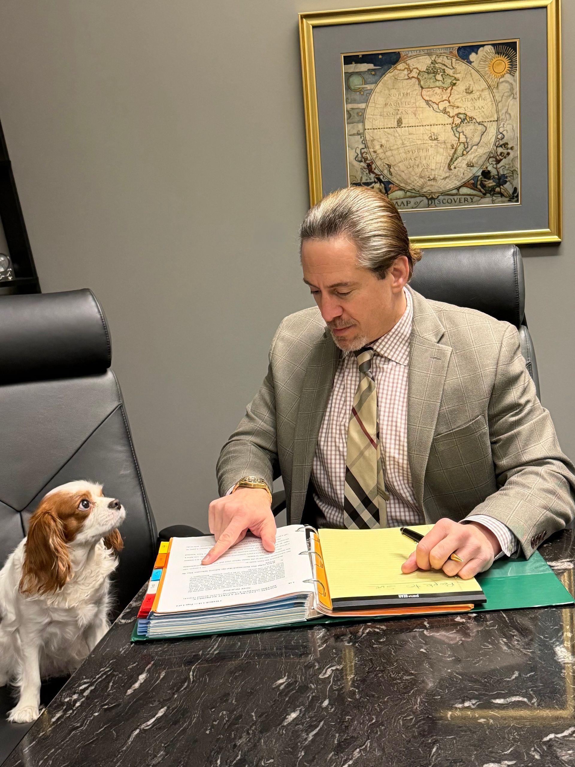 Woman in blue blazer smiles while on phone and using a tablet in a cafe, with coffee and water on the table.