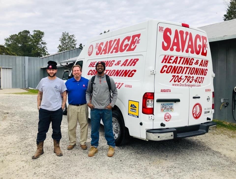 Three men are standing in front of a savage heating and air conditioning van.