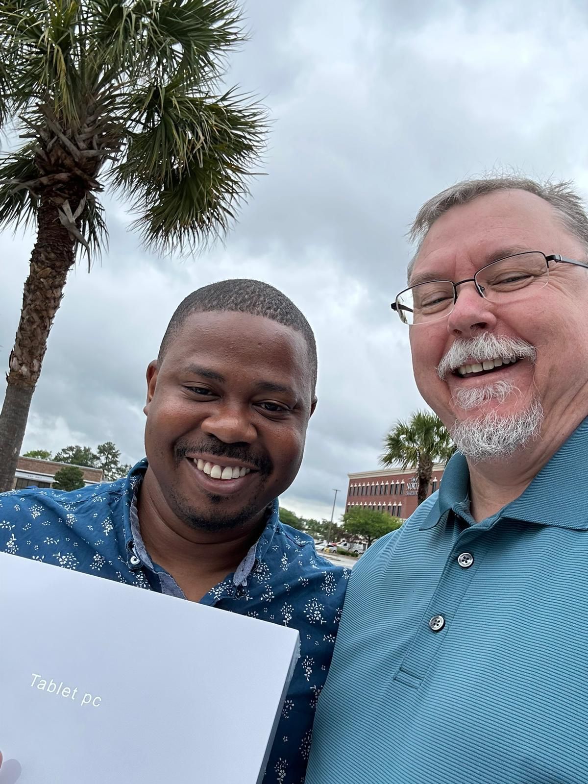 Two men are posing for a picture in front of a palm tree.