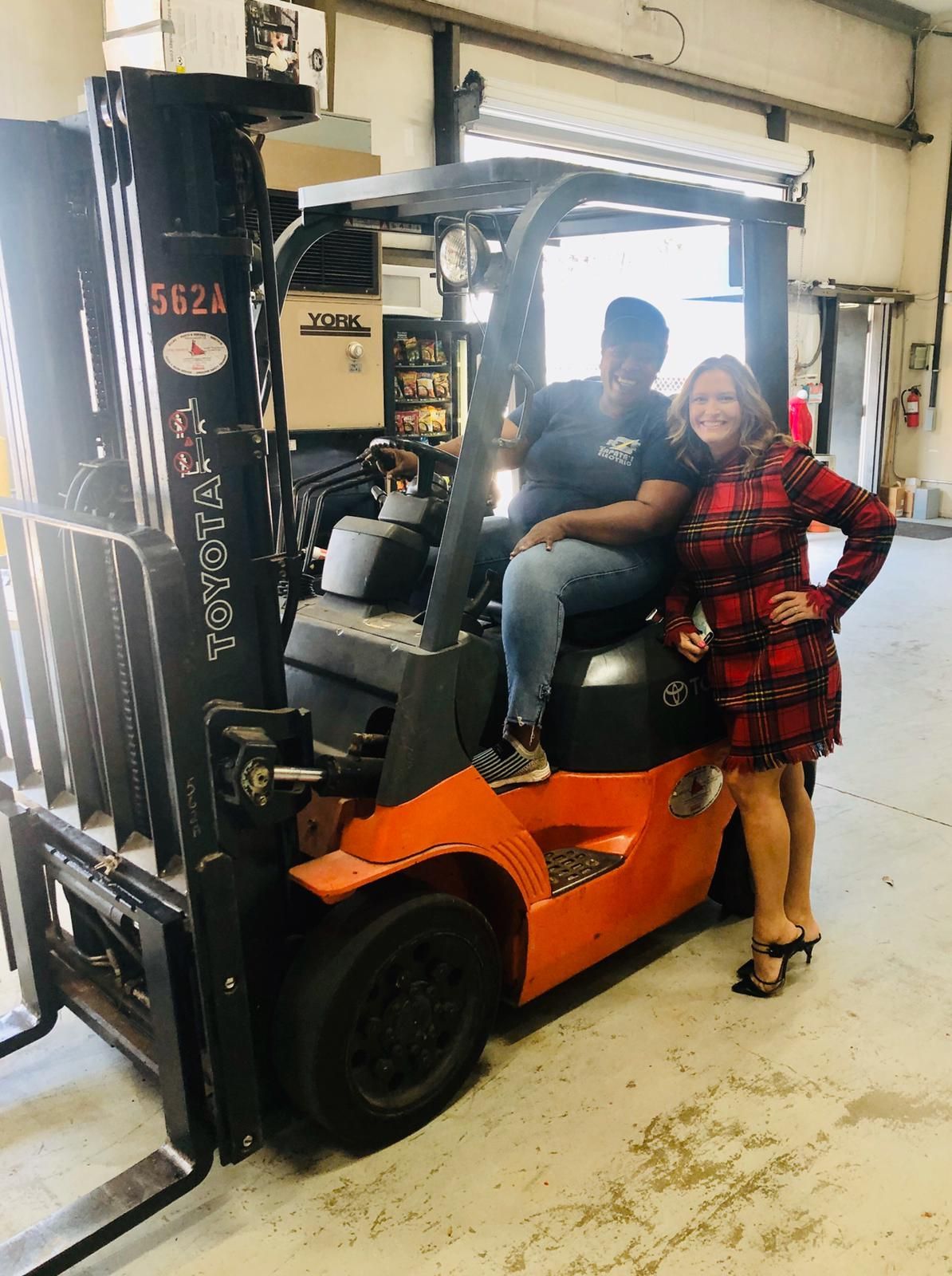 Two women are standing next to a forklift in a garage.
