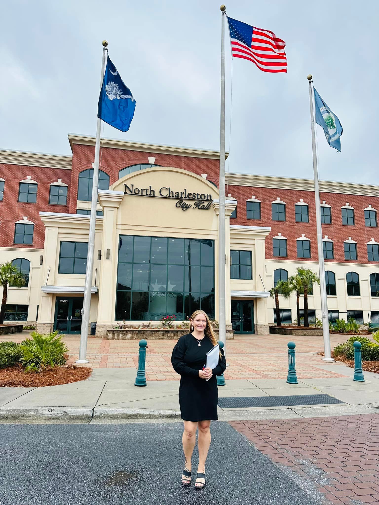 A woman is standing in front of a large building with flags.