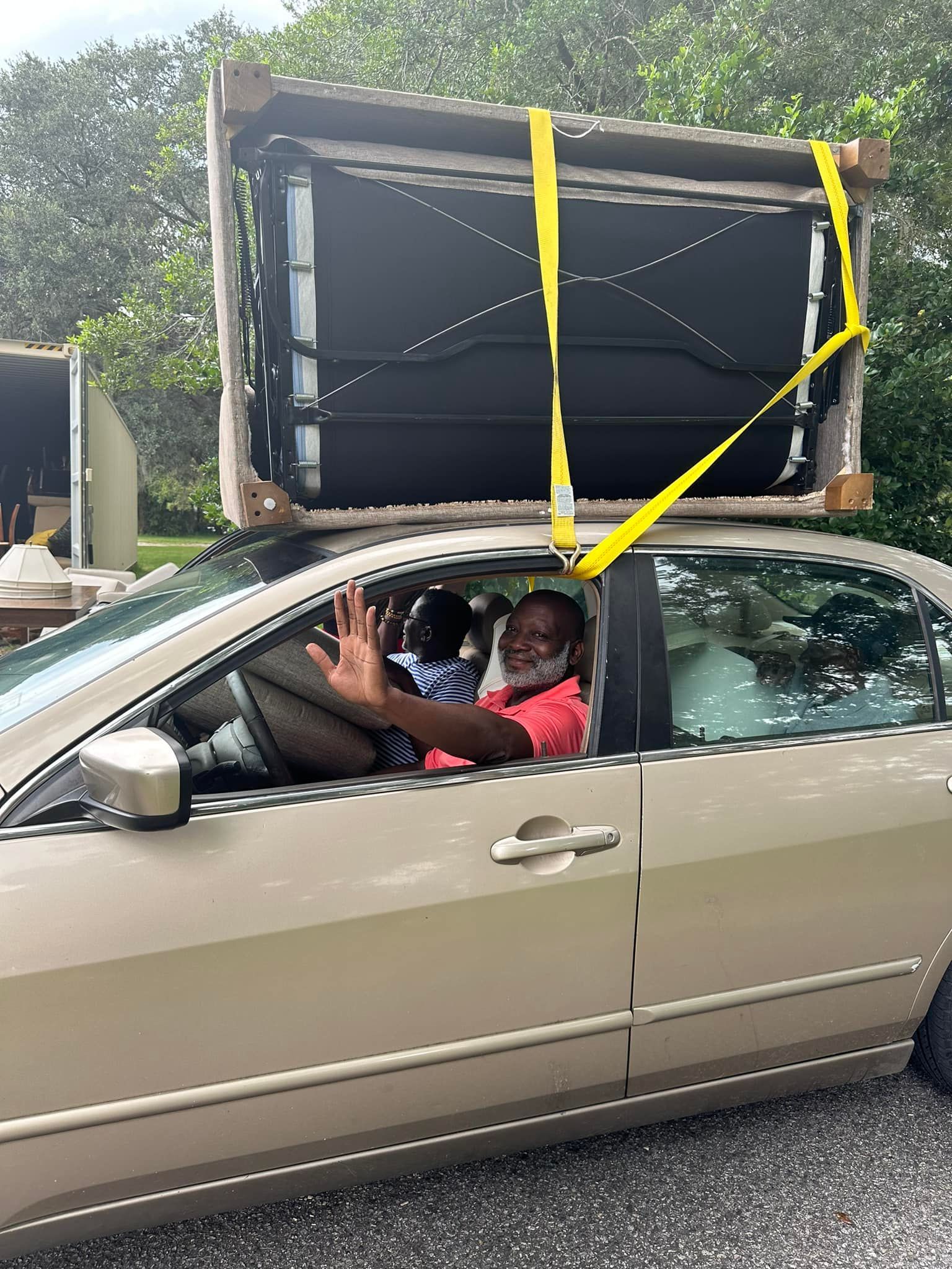 A man is driving a car with a couch on top of it.