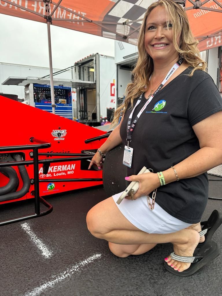 A woman is kneeling down in front of a red race car.