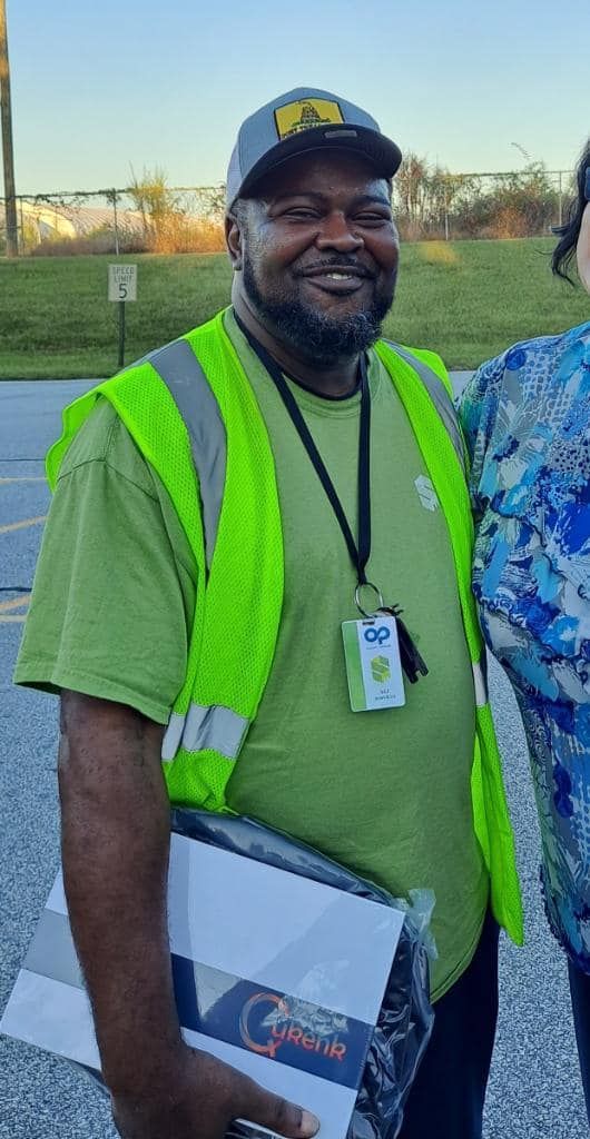 A man wearing a green shirt and a yellow vest is standing next to a woman.