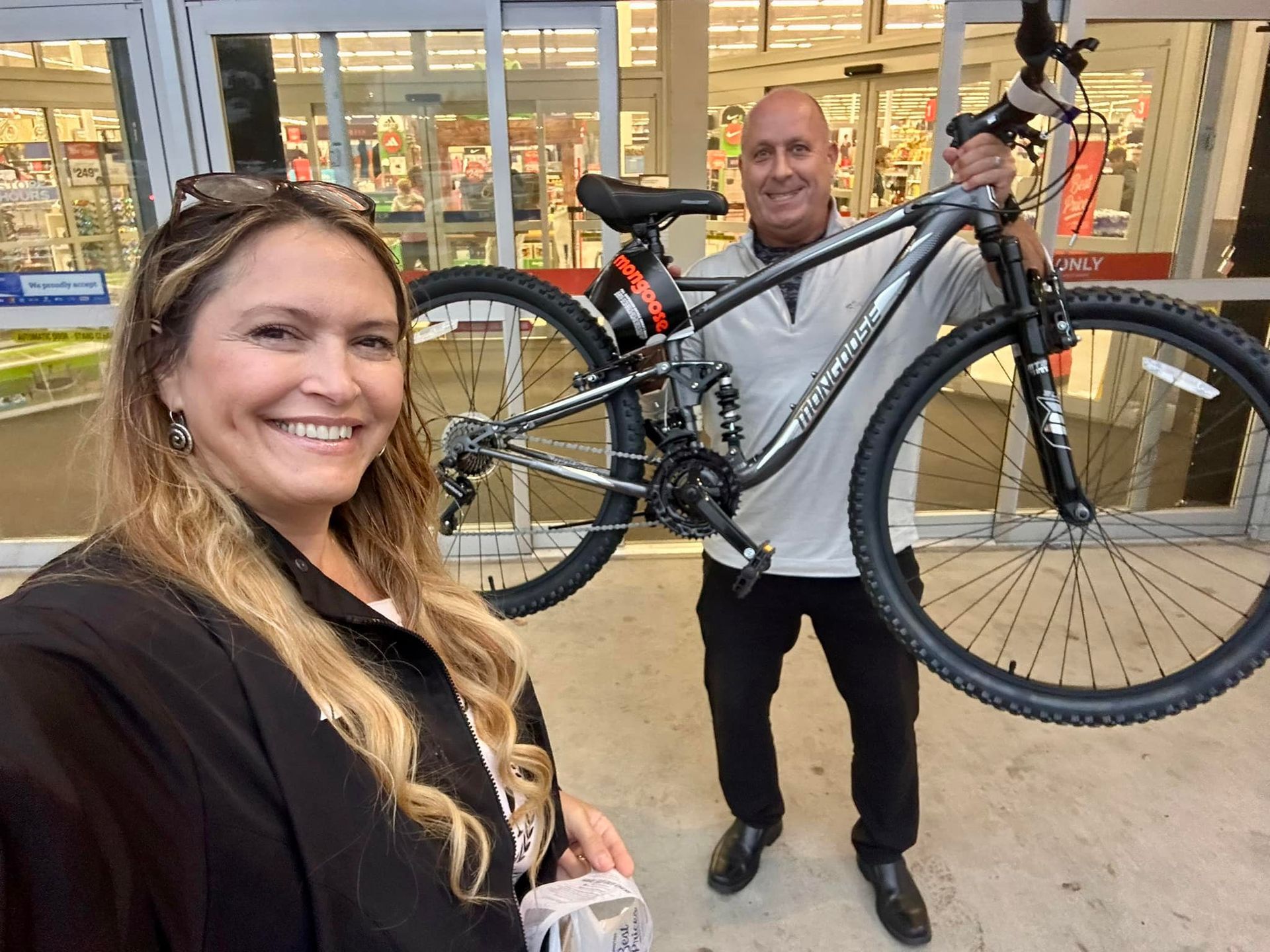 A man and a woman are holding a bicycle in front of a store.