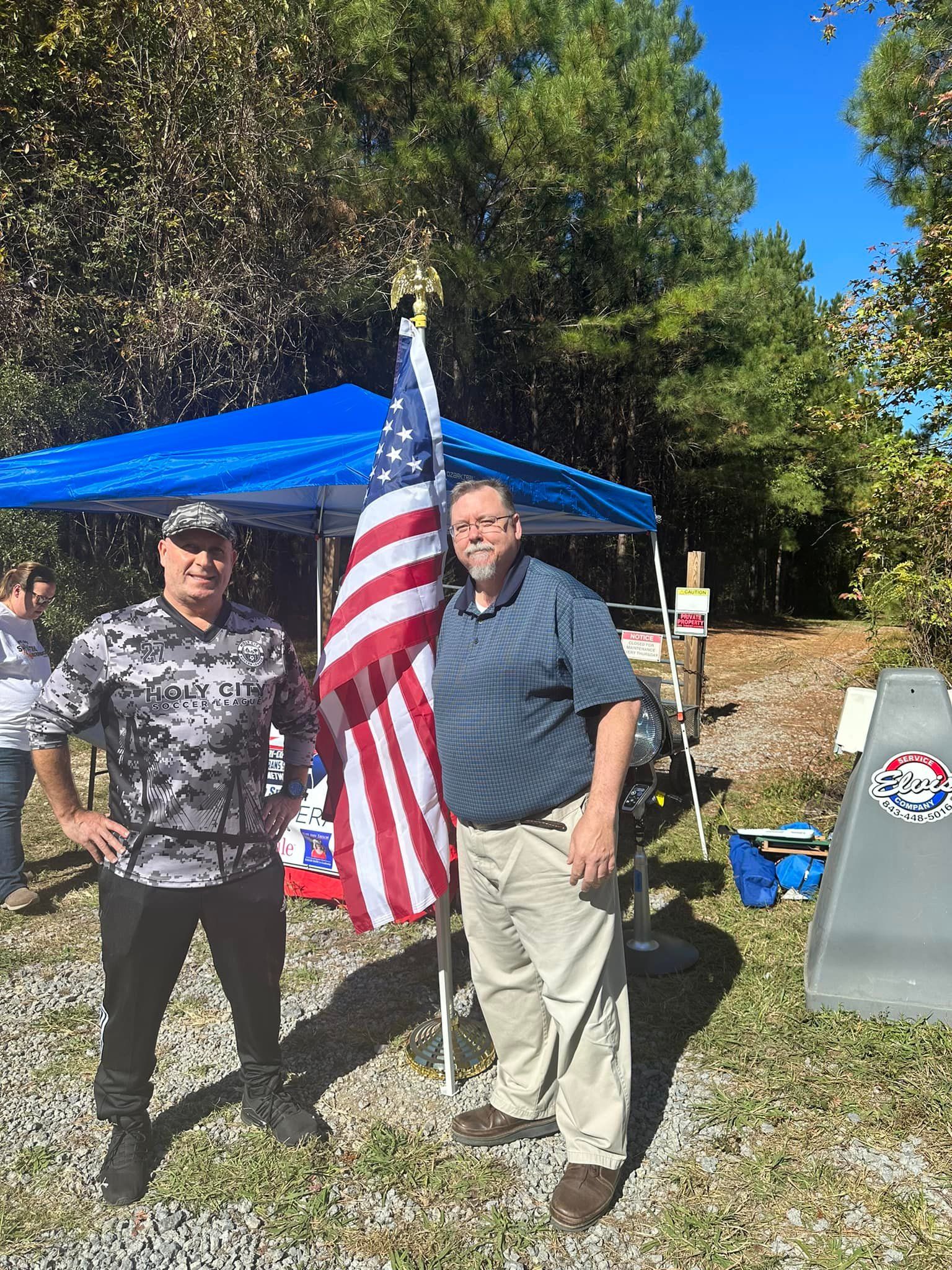 Two men are standing next to each other in front of an american flag.