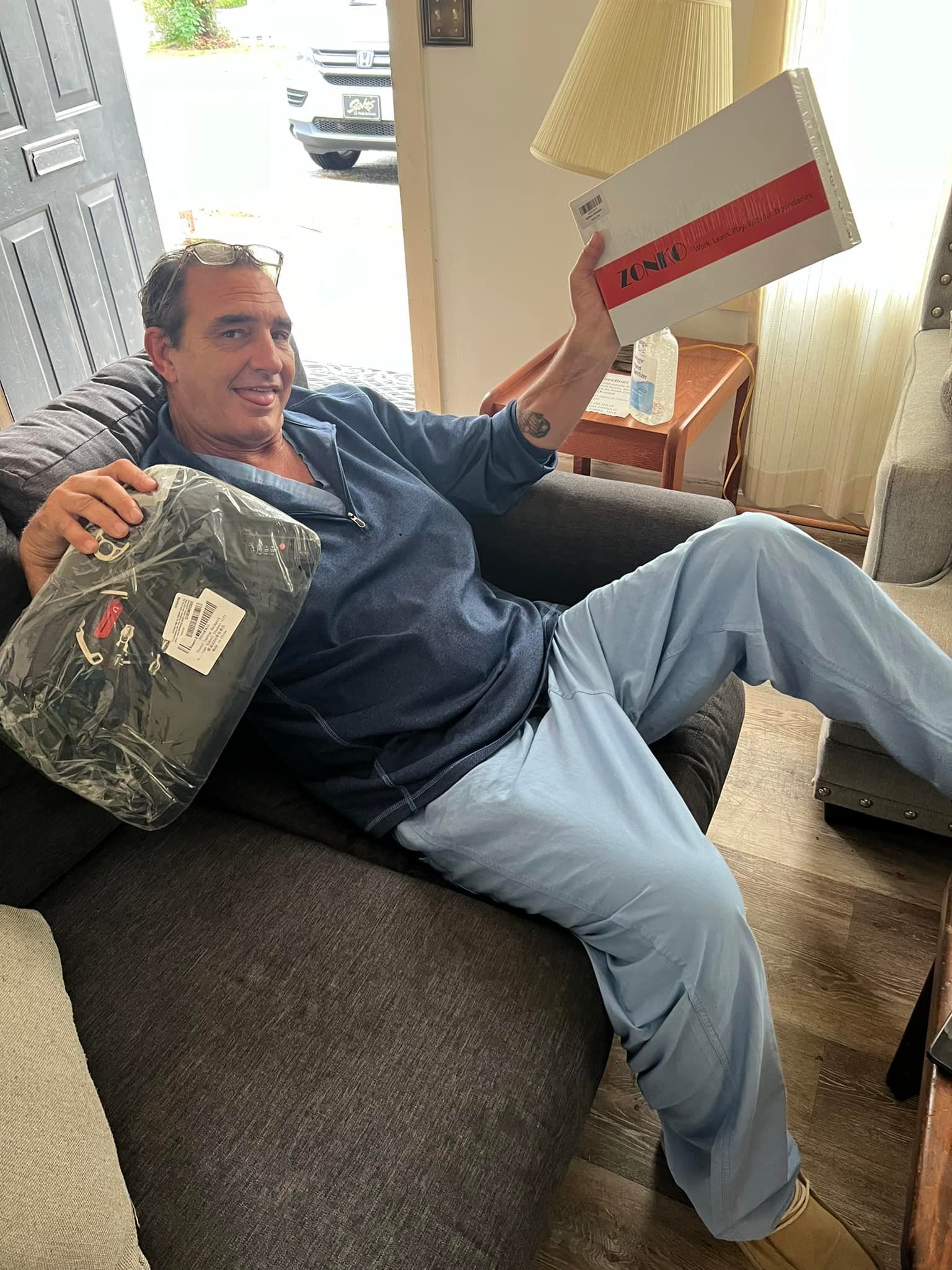 A man is sitting in a chair holding a box and a pillow.