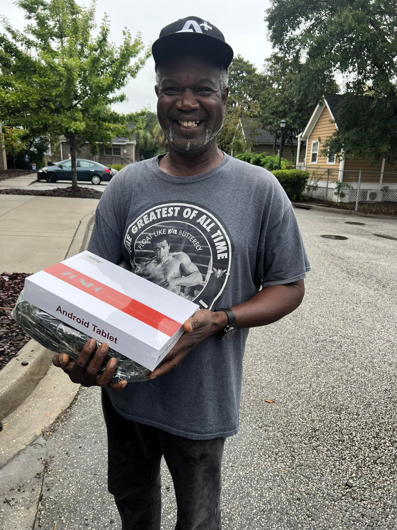 A man in a gray shirt is holding a box and smiling.