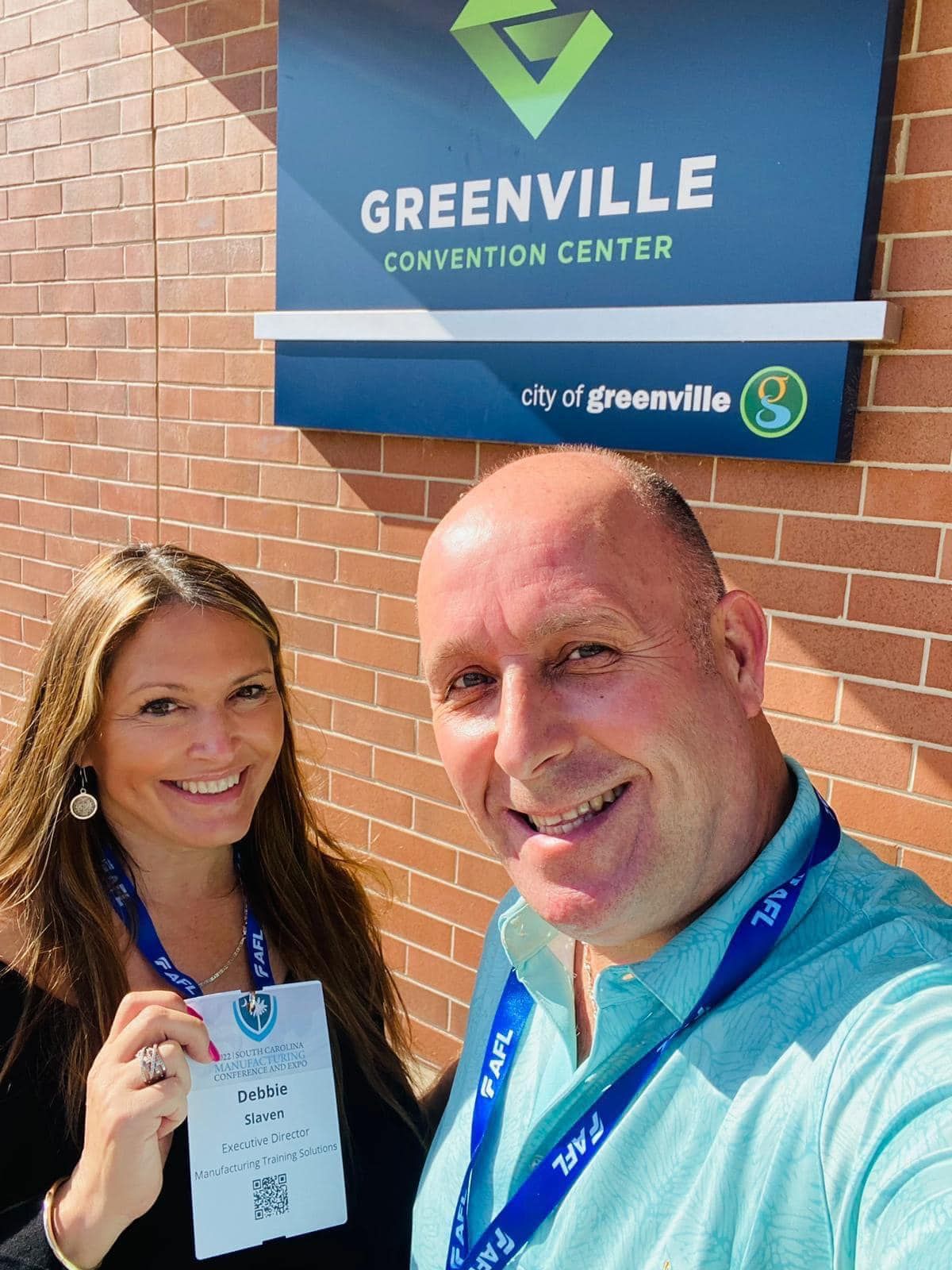 A man and a woman are posing for a picture in front of a greenville convention center sign.