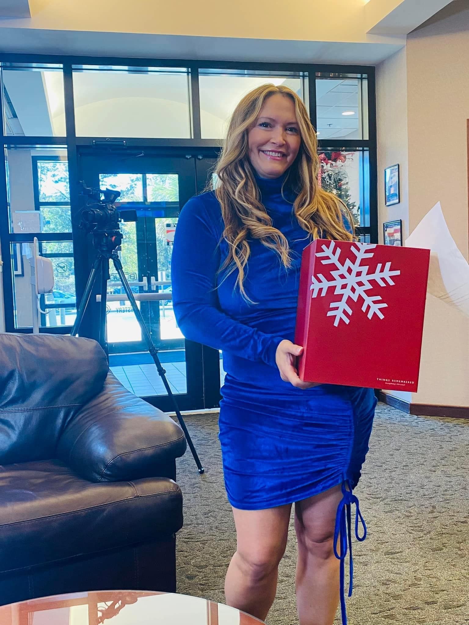 A woman in a blue dress is holding a red bag with a snowflake on it.