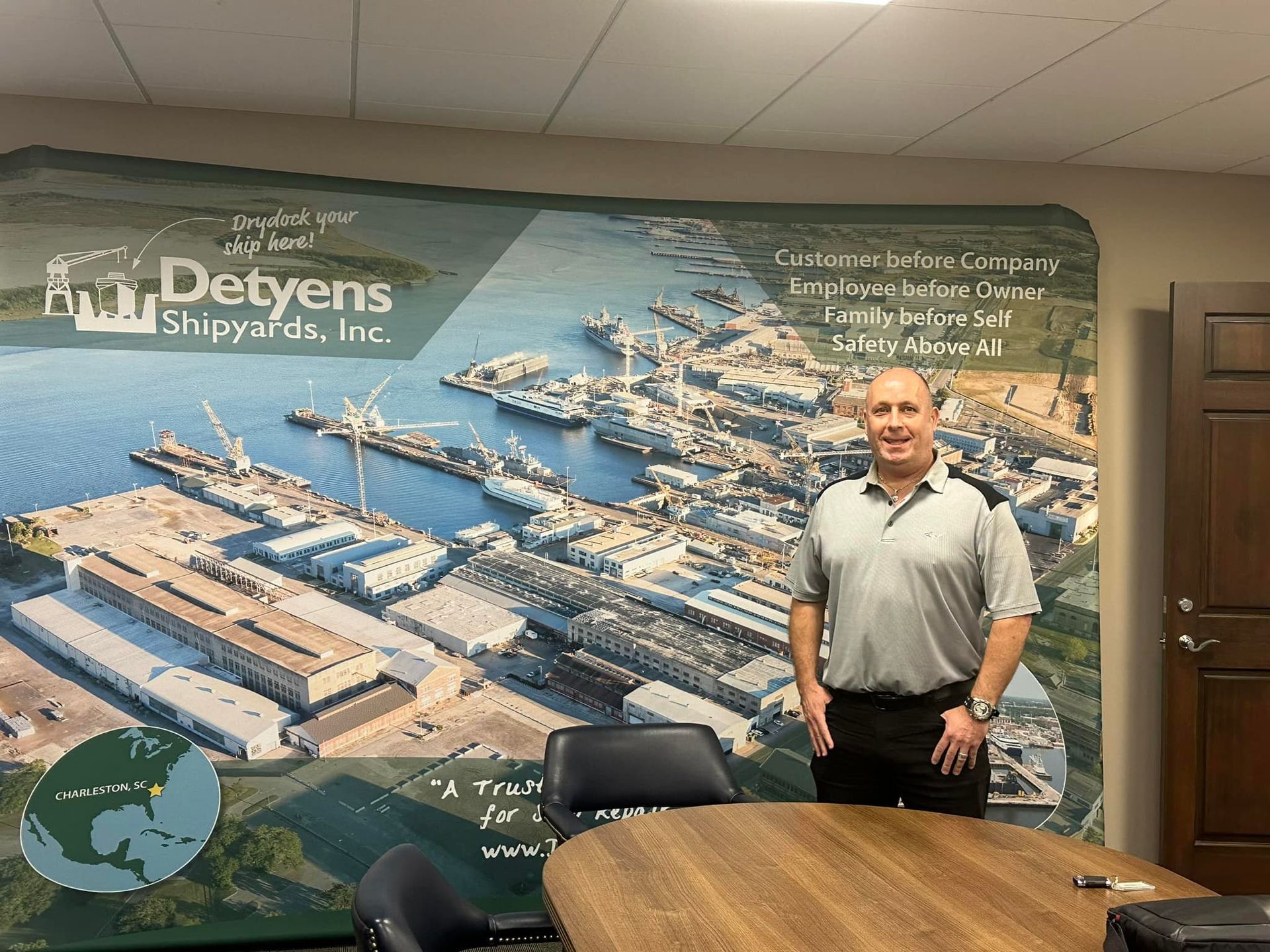 A man is standing in front of a wall with a picture of a shipyard on it.