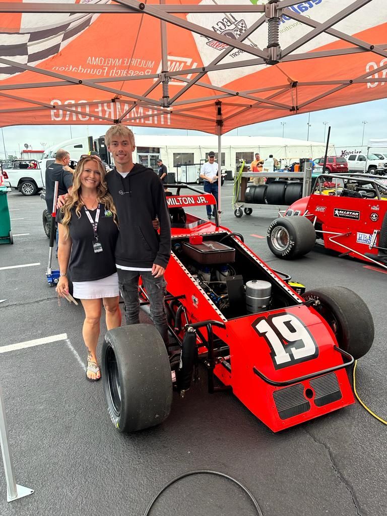 A man and a woman are standing next to a red race car with the number 19 on it.