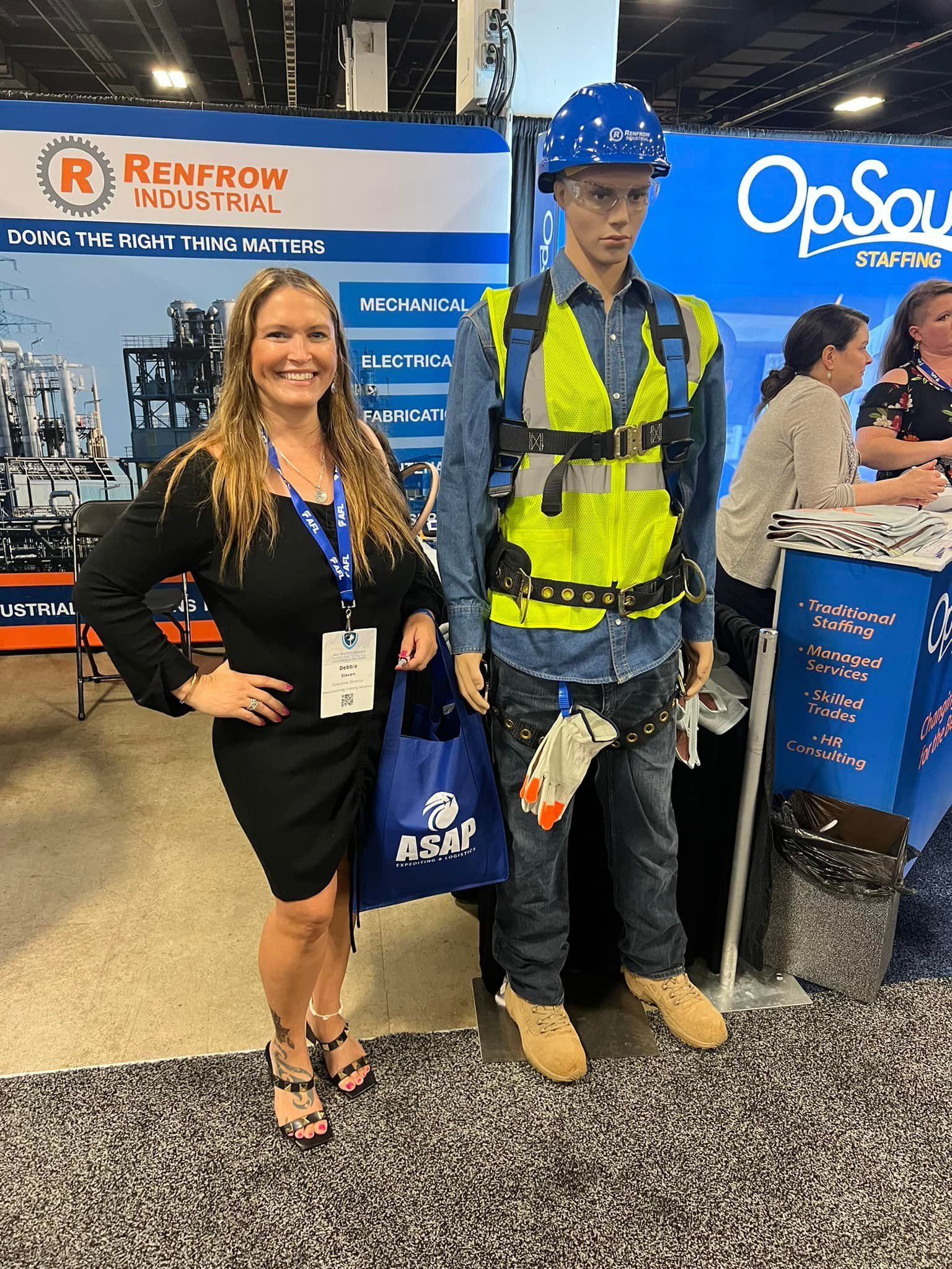 A woman is standing next to a mannequin wearing a hard hat and safety vest.